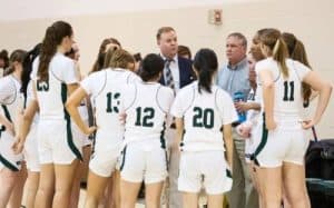 Prepared female volleyball team listening to coaches during timeout at a game.