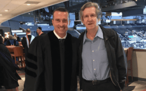Chris Herren at graduation ceremony in academic regalia with a guest.
