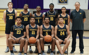 Massanutten basketball team and coach pose in black and gold uniforms for a formal group photo inside the gym, seated and standing in two rows.