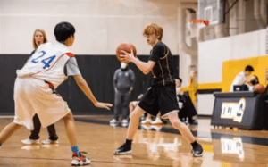 Tilton School basketball player in black uniform holding the ball against a defender during a NEPSAC prep school game.