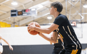 Tilton School basketball player in black and yellow uniform holding the ball during a prep school game.