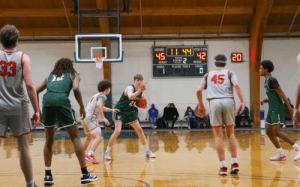 Winchendon School basketball player (#21) setting up offense against defender in prep school game with scoreboard showing close score