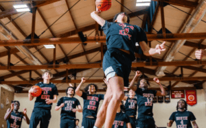 South Kent basketball player dunks during practice as teammates cheer, showcasing prep school athletic intensity and development.