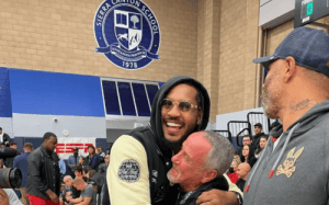 Steve Smith hugging Carmelo Anthony courtside at Sierra Canyon School basketball game surrounded by fans and media