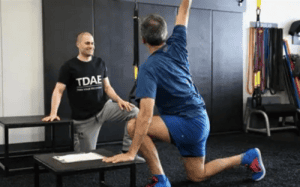 Tim DiFrancesco coaching an athlete through a recovery and mobility exercise in a training facility.