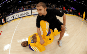 Tim DiFrancesco assisting a Lakers player with on-court recovery and stretching during pre-game preparation. 