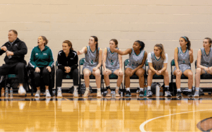 Western Reserve Academy girls basketball players and coaches watch the game from the bench during prep school competition.