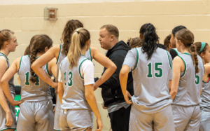 Coach Thomas Adams-Wall talks to the Western Reserve Academy girls basketball team during a prep school game huddle.
