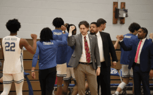Blue Ridge School basketball coaching staff and players raise their fists together in unity during a timeout, demonstrating teamwork and leadership.
