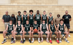The 2023–24 Deerfield Academy boys basketball team poses together in green uniforms with coaches and staff in the gym, representing the Big Green program.