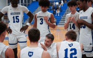 Mercersburg Academy basketball coach gives instructions to players in a huddle during a timeout, emphasizing teamwork and strategy in a prep school basketball game.