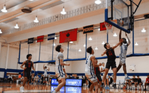Mercersburg Academy basketball player goes up for a layup against defenders during a prep school basketball game inside the campus gym with banners hanging above the court.