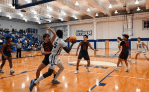 Mercersburg Academy basketball player drives toward the basket against defenders during a prep school game as teammates and fans watch inside the Storm gym.