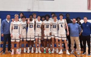 The Mercersburg Academy boys basketball team stands together on the court with coaches, wearing white uniforms and showing unity and confidence after a prep school game.