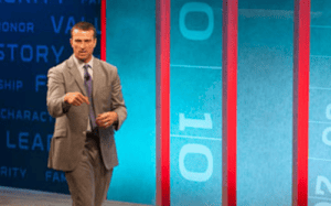 Chris Herren delivers a motivational speech on athlete character, values, and mental wellness on a brightly lit stage.