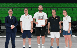 Coach Nemo Maric stands with fellow coaches and officials while receiving an EHCB certification award inside an arena.