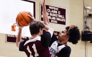 NEPSAC prep school basketball players contesting a shot at the rim during a high-intensity game in a high school gym.