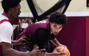 Prep school basketball player protecting the ball through contact while being defended in a physical half-court possession.