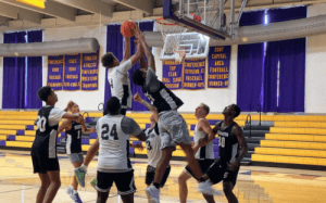 Prep school basketball players competing for a rebound under the rim during a game, showing physicality, timing, and in-game effort.