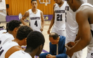 Prep school basketball coach drawing up a play during a timeout while players listen closely, emphasizing instruction, focus, and in-game learning.